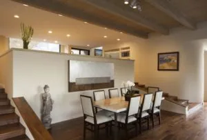 Modern dining room with light wood table, upholstered chairs, exposed beam ceiling, and white accent walls with artwork