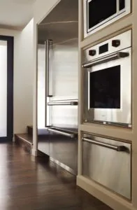 Modern kitchen with stainless steel appliances, glass refrigerator doors, and built-in oven on cream cabinetry with dark wood flooring