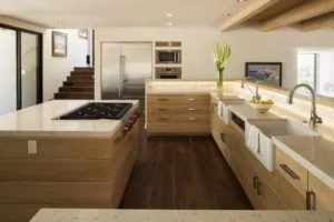 Modern kitchen with light wood cabinetry, stainless steel appliances, marble countertops, gas cooktop island, and dark wood flooring.