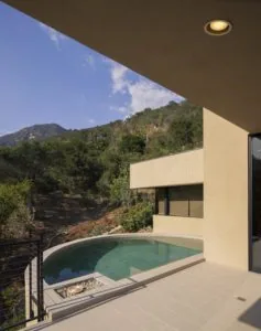 Modern house with turquoise pool overlooking forested hillside with recessed ceiling light