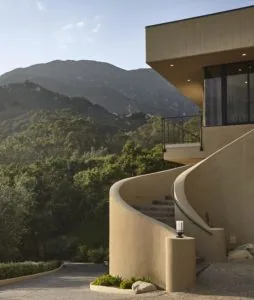 Modern curved concrete residential building with balcony overlooking forested mountain valley