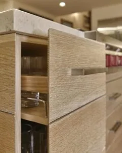 Light wood kitchen cabinetry with open drawer and marble countertop in modern home interior
