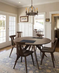 Round dining table with dark wood chairs and blue placemats in bright room with chandelier and glass doors