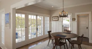 Dining room with dark wood table, mid-century chairs, and glass doors opening to deck with water view