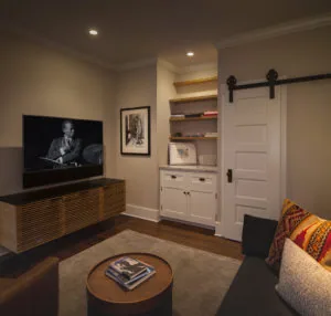 Modern home theater room with wall-mounted TV, wood media console, built-in shelving with barn door, round coffee table, and upholstered seating
