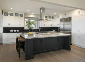 Modern kitchen with white cabinetry, black island with marble countertop, stainless steel appliances, and hardwood flooring