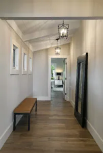 Bright hallway with vaulted ceiling, pendant lights, wooden bench, and view into adjacent room through open doorway