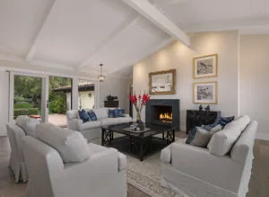 Modern living room with white coffered ceiling, fireplace, gray upholstered seating, black coffee table, and view to patio