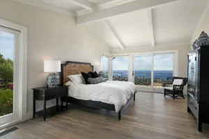 Modern bedroom with black bed, white bedding, hardwood floors, and ocean views through large glass doors