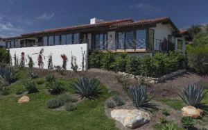 Modern white stucco house with terracotta tile roof and extensive windows, landscaped front yard with agave plants and decorative rock