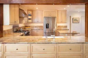 Modern kitchen with light wood cabinetry, granite countertops, stainless steel refrigerator, and island seating
