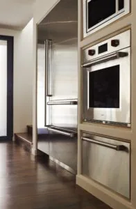 Modern kitchen with stainless steel appliances, glass-front refrigerator, and built-in oven next to wood flooring