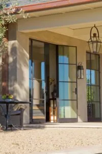 Contemporary patio with tan stucco exterior, black-framed glass doors, hanging lanterns, and gravel flooring
