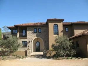 Mediterranean-style home exterior with stone and stucco facade, arched entryway, clay tile roof, and olive trees