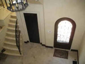 Entryway with arched doorway featuring decorative ironwork, dark door, staircase with black railing, and tile flooring.