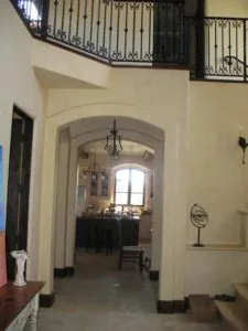 Cream-colored hallway with arched doorways, decorative wrought iron railings visible above, and pendant lighting fixtures