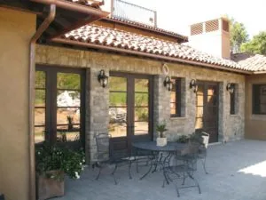 Stone patio with dark-framed French doors, metal outdoor furniture, and Spanish tile roof overhang