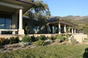 Modern house with concrete and wood exterior, covered porch with columns, drought-resistant landscaping, and mountains visible in background