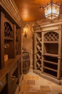 Ornate wine cellar with wooden cabinetry, latticed doors, stone flooring, and decorative wrought iron pendant lighting