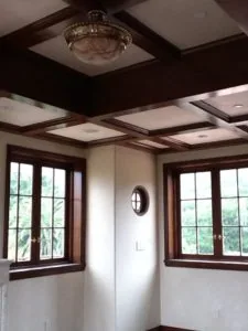 Interior room with coffered ceiling, dark wood beams, recessed lighting, and French doors with gridded windows overlooking trees