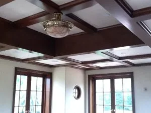 Coffered ceiling with dark wood beams, skylight panels, and brass flush-mount light fixture above glass-paned doors