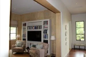 Living room with wooden built-in entertainment center, upholstered armchairs, bookshelves, television, and large windows