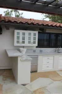 Outdoor kitchen with white cabinetry, stone countertops, built-in grill, and clay tile roof under covered patio