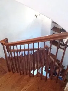 Wooden staircase with turned balusters and handrail viewed from above, white walls and wooden flooring visible