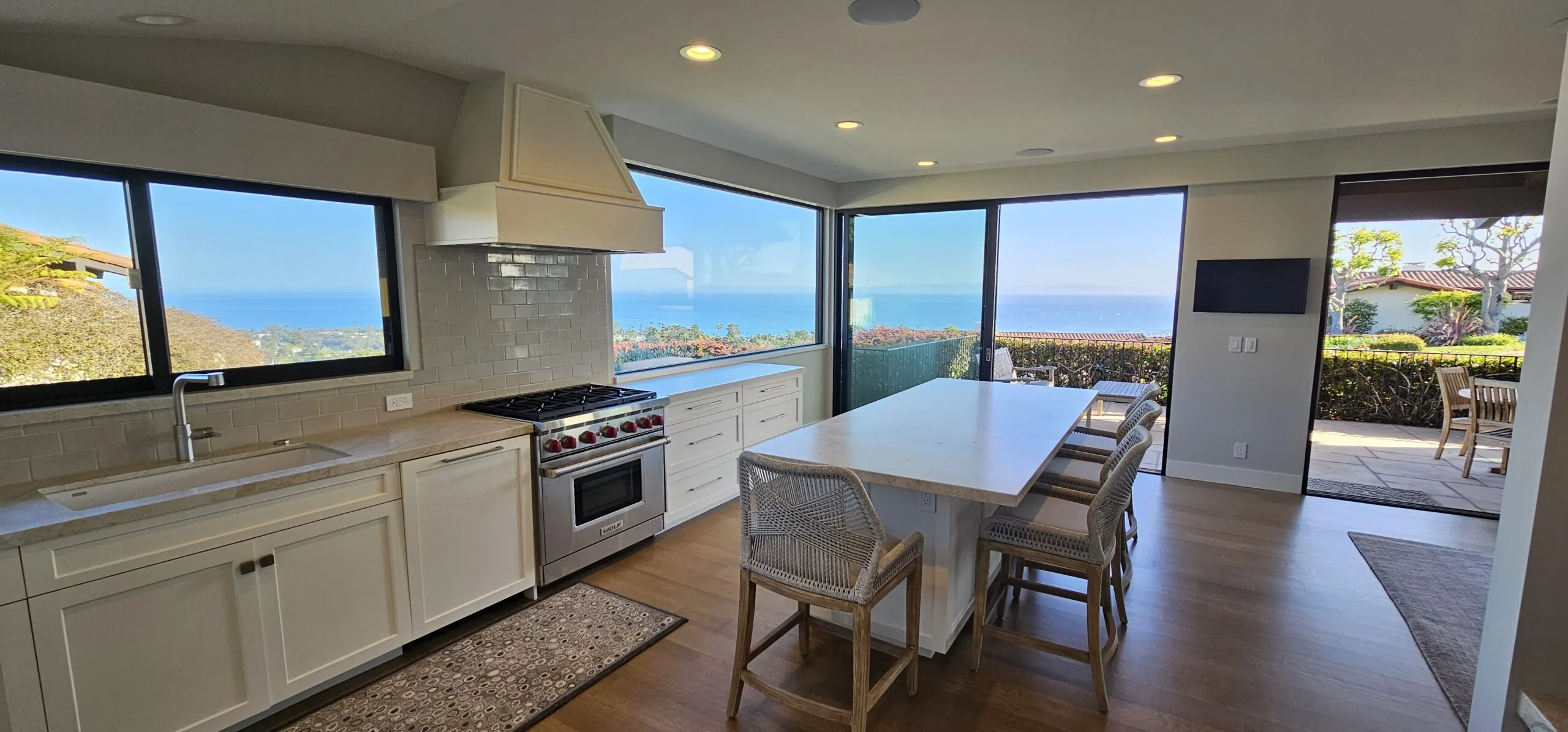 Modern kitchen and dining area with white cabinetry, stainless steel appliances, island seating, and expansive ocean views through floor-to-ceiling windows