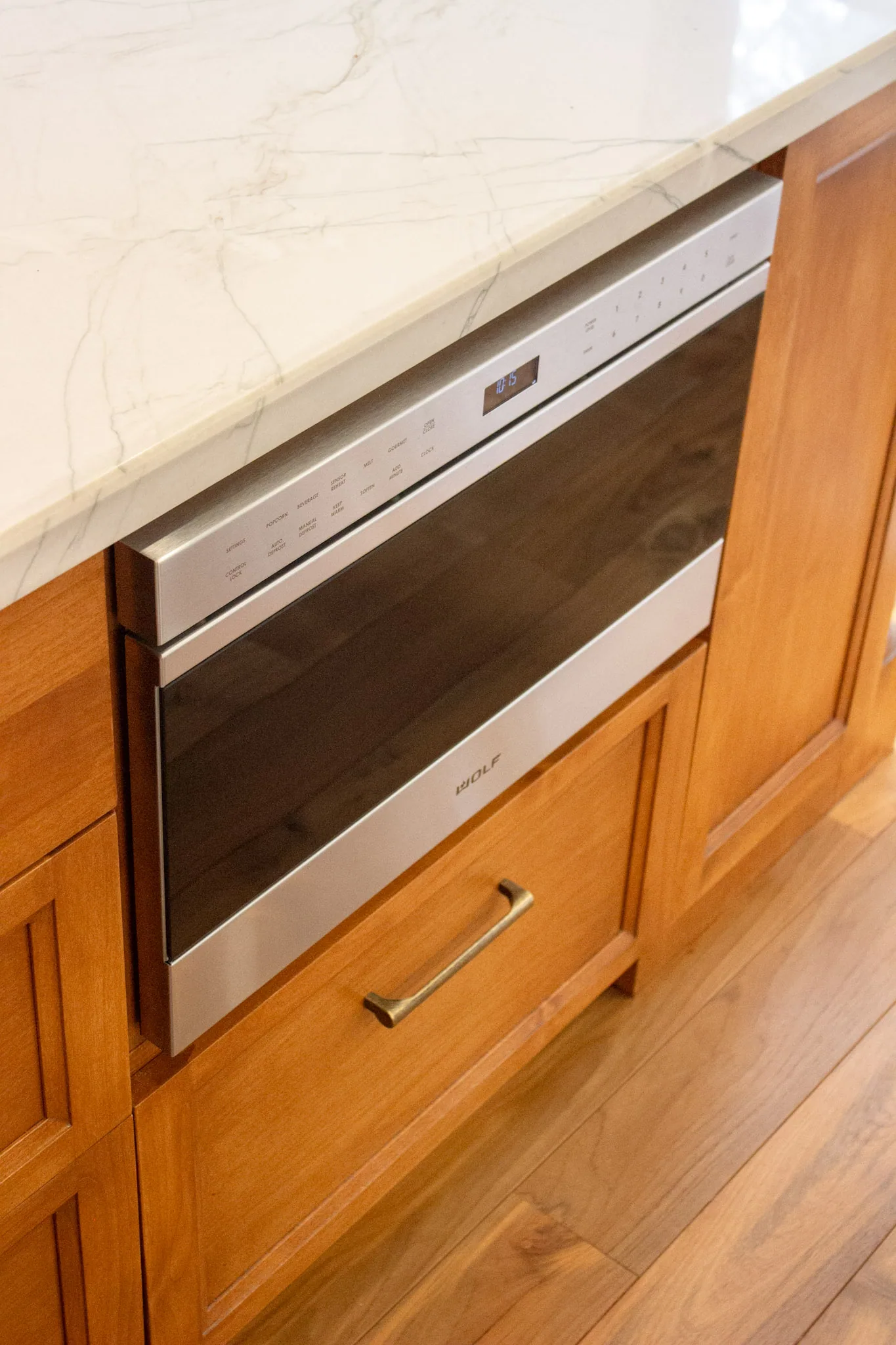 Stainless steel wall oven installed in wood cabinetry below cream marble countertop