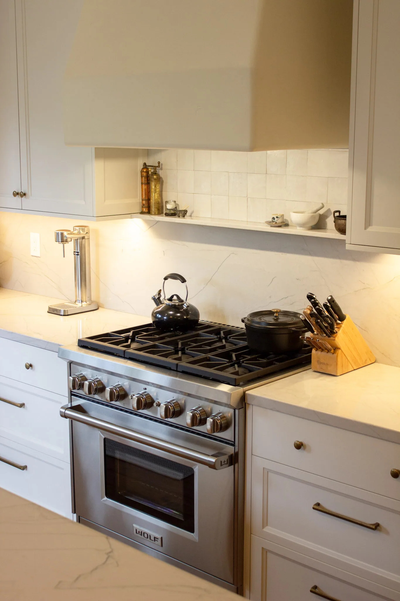 Modern kitchen with white cabinetry, marble countertops, stainless steel range with gas cooktop, white subway tile backsplash, and warm lighting