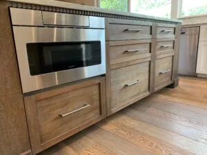 Kitchen island with stainless steel microwave, wood cabinetry, and metal handles under natural light