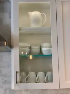 White ceramic dishes and pitcher displayed on shelves in a glass-front cabinet