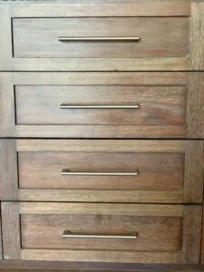 Four wooden drawers with metal bar handles stacked vertically in light to medium brown wood grain
