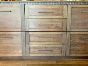 Wooden kitchen cabinet with four stacked drawers and metal handles, showing medium to dark wood stain finish.