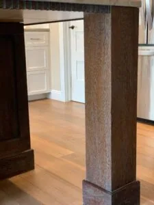 Kitchen with dark wood support column on light wood flooring, white cabinetry visible in background