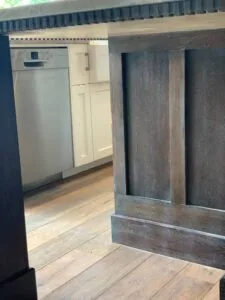 Kitchen interior with white dishwasher, cream cabinets, dark wood-grain cabinetry, and light wood flooring