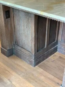 Wooden kitchen island with dark stained base and textured panel doors, decorative trim along top edge, on hardwood floor