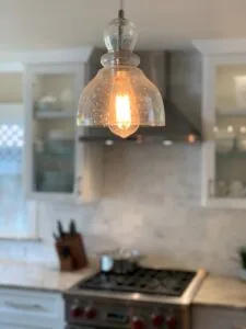 Clear glass dome pendant light with warm bulb hanging above kitchen counter with stove