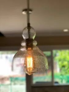 Hanging glass pendant light with glowing filament bulb and metal cross finial