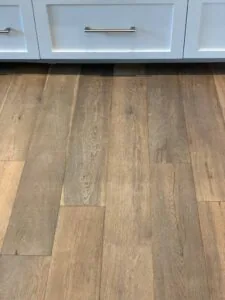 White kitchen cabinets with glass doors above wide plank hardwood flooring
