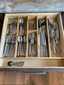 Organized flatware drawer with multiple compartments holding forks, spoons, and knives in a wooden organizer tray with measuring spoons at the bottom.